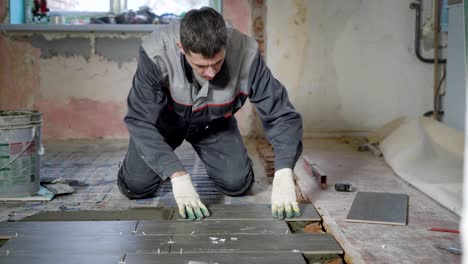 experienced-worker-is-doing-tiling-work,-is-lying-grey-tiles-on-a-floor-in-an-office-room-with-window