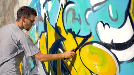 Graffiti-artist-is-painting-a-black-triangle-on-the-yellow-letter,-right-view.