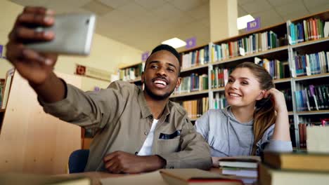 Afrikanische-Merican-Kerl-und-kaukasische-Mädchen-viel-Spaß-beim-Lächeln-und-Selfie-Fotos-auf-Smartphone-Kamera-an-der-Universitätsbibliothek.-Fröhlichen-Studenten-haben-Pause,-während-für-die-Prüfung-vorbereiten