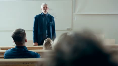 Clase-de-frente-a-cámara:-Prominente-profesor-escribiendo-en-la-pizarra-y-dar-Conferencia-a-una-clase-de-estudiantes-Multi-étnica.-Universidad-moderna-con-jóvenes-brillantes.