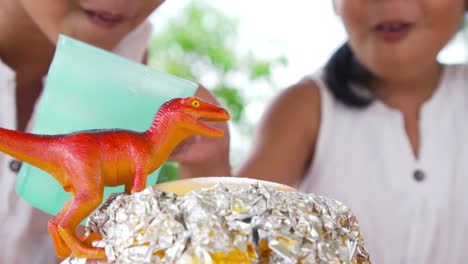 Two-asian-little-girls-do-the-baking-soda-and-vinegar-volcano-experiment-at-the-table-in-their-house,-slow-motion-in-50-fps