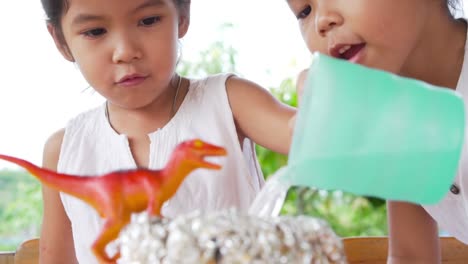 Two-asian-little-girls-do-the-baking-soda-and-vinegar-volcano-experiment-at-the-table-in-their-house,-slow-motion-in-100-fps