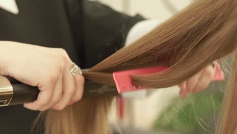 Estilista-con-pinzas-de-pelo-y-peine-para-el-cabello-alisado-modelo-en-el-salón-de-belleza.-Peluquería-alisar-el-cabello-largo-durante-la-Peluquería-mujer-en-peluquería-de-cerca