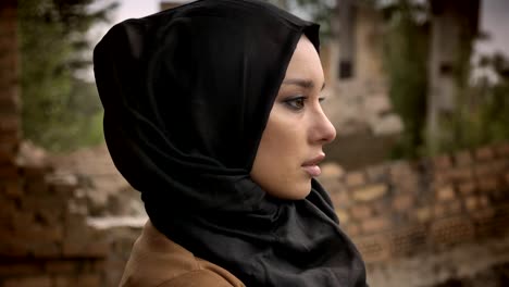 Joven-musulmana-hijab-mirando-lejos-y-al-cámara,-preocupada-y-con-miedo,-arruinado-edificio-de-fondo