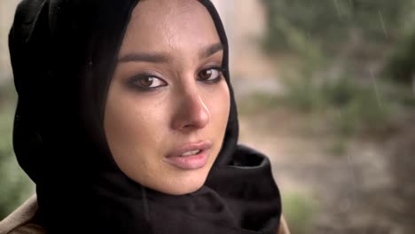 Portrait-of-young-muslim-woman-in-hijab-looking-at-camera-with-sad-depressed-expression-during-rain