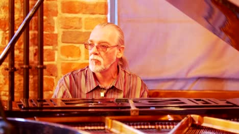 A-gray-haired-man-with-a-tail-on-his-head-wearing-glasses-enthusiastically-and-thoughtfully-plays-the-piano-in-a-jazz-bar