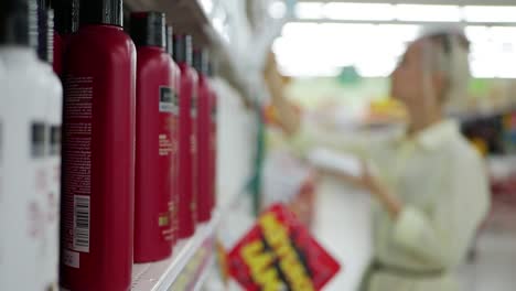 Mujer-joven-borrosa-elegir-acondicionador-o-shampoo-en-una-tienda-de-belleza.-Mujer-que-sostiene-un-producto-de-cuidado-del-cuerpo