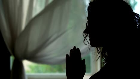 Woman-silhouette-praying-indoors,-reading-a-pray-with-hands-folded,-asking-God