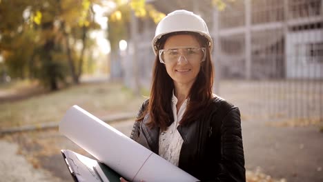 Portrait-of-Happy-professional-construction-engineer-woman-holding-the-blueprint-and-wearing-the-safety-helmet-and-glasses.