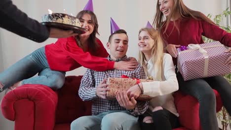 Handsome-man-blowing-birthday-candles-while-close-friends-throwing-a-surprise-party,-slowmotion-in-cozy-modern-apartment