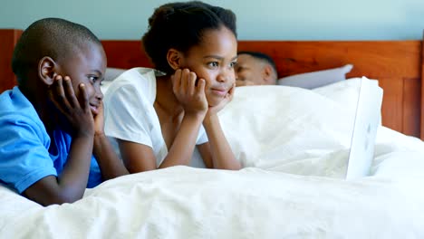 Seitenansicht-des-schwarzen-Kindern-am-Bett-liegen-und-Blick-auf-Laptop-im-Schlafzimmer-bequem-nach-Hause-4-k