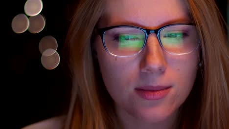 Close-up-footage-of-spectacled-caucasian-blonde-woman,-looking-at-computer-screen-and-it-is-reflected-in-her-glasses,-dark-background,-focused-person,-smart-vibes