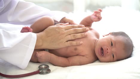 4K-Medium-close-up-shot-female-pediatrician-doctors-hand-consoling-crying-asian-newborn-baby-girl-using-stethoscope-listening-to-little-baby-girl-heartbeat-for-medical-exam.-Hospital-nursery-healthcare-concept.