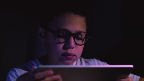 Lindo-niño-usando-tableta-en-la-habitación-oscura