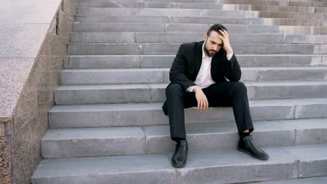 Upset-young-business-man-having-stress-and-sitting-on-stairs-in-street.-Businessman-having-deal-problems-concept