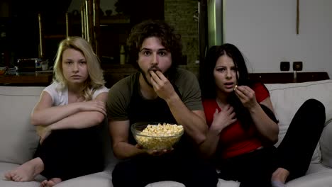 Two-young-women-and-a-guy-eating-popcorn-and-watching-horror-film-with-a-fear-grim-on-their-face