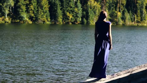 Slowmotion-of-Beautiful-young-woman-in-long-dress-standing-on-shore-near-lake