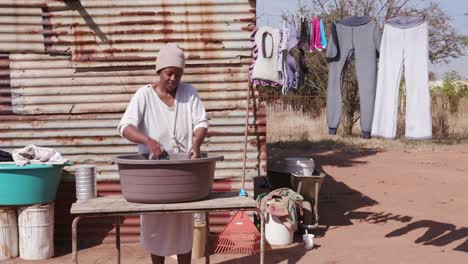 Afrikanische-Frau-ohne-fließendes-Wasser,-Wäsche-in-einem-Eimer-vor-ihrem-Hause-Blechhütte