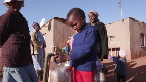 Afrikanischen-jungen-sammeln-von-Wasser-aus-einem-Hahn,-während-Frau-Line-up,-Wasser-in-Plastikbehältern-aufgrund-der-schweren-Dürre-in-Südafrika-zu-sammeln