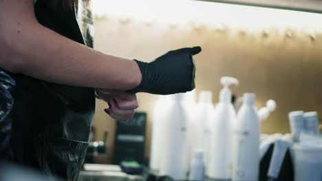 Hairdresser-puts-on-black-gloves-before-strarts-working-in-beauty-salon.-Closeup-view