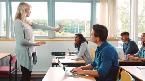 Female-Tutor-Standing-To-Teach-Class-Of-Mature-Students