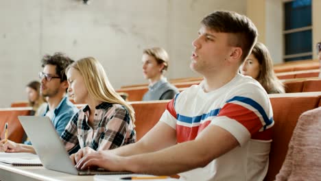 Gut-aussehend-kaukasischen-Student-nutzt-Laptop-beim-Hören-eines-Vortrags-an-der-Universität,-er-wirft-Hand-und-fragt-Dozent-einer-Frage.-Multi-ethnischen-Gruppe-von-modernen-hellen-Studenten.