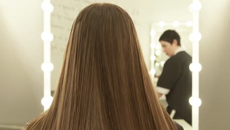 Hairstylist-combing-long-hair-for-making-woman-hairdo-front-mirror-in-beauty-salon.-Close-up-female-hairstyle-in-beauty-salon