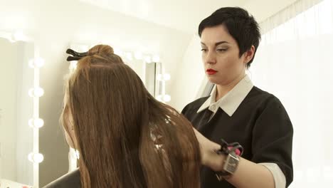 Peluquería-mujer-peinándose-el-cabello-largo-para-mujer-corte-de-pelo-delante-del-espejo-en-salón-de-belleza.-Cierre-haircutter-partiendo-el-pelo-antes-de-cortar.-Peinado-femenino-en-salón-de-peluquería