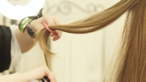 Friseur-mit-Zange-Haar-und-Kamm-für-Hairstyling-im-Beauty-Salon.-Richten-Sie-lange-Haare-im-Friseursalon-Friseur-hautnah