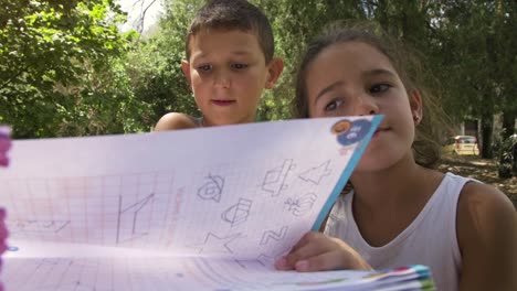 Young-kids-in-summer-camp-doing-homeworks-outside-outdoor-in-park-under-trees-sitting-on-table-lying-on-ground-slow-motion