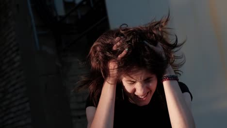 A-young-woman-stands-in-front-of-abandoned-factory,-emotively-dissaranges-her-hair-and-cries,-feeling-guilty-for-something