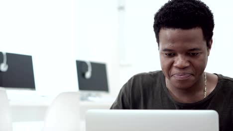 Handsome-Black-university-student-smiling-and-laughing-while-working-on-laptop-in-computer-classroom