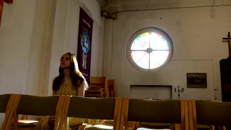 Young-caucasian-religious-devoted-woman-on-the-bench-in-Catholic-Church