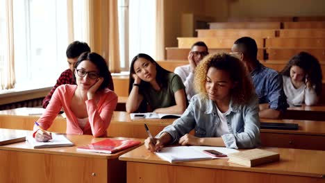 Müde-und-gelangweilt-Schüler-Lehrer-anhören-und-Notizen-in-Notizbüchern-sitzen-am-Schreibtisch-in-der-Universität.-Bildung,-Langeweile,-junge-Menschen-und-Klassenzimmer-Konzept.