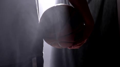 Close-footage-of-basketball-player-holding-ball,-standing-in-dark-misty-room