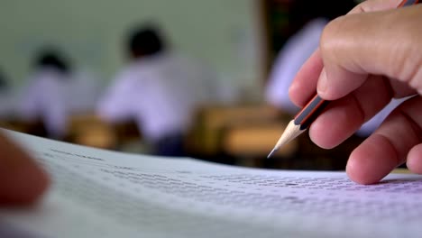 Bildung-Testkonzept:-Hände-Schüler-halten-Stift-für-Prüfung-Prüfungen-schreiben-Antwortbogen-oder-Übung-für-die-Aufnahme-in-Prüfung-Kohlepapier-Computer-auf-Holztisch-im-Klassenzimmer-in-der-High-School-zu-füllen