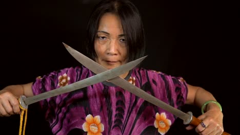 slow-motion-old-intimidating-asian-woman-crosses-swords-with-black-background