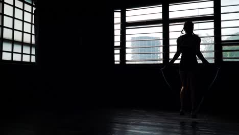 silhouette-panning-young-purposeful-female-boxer-in-wrapped-bandage-hands-jumping-on-skipping-rope