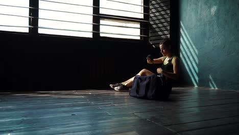 Slow-motion-panning-fit-young-woman-with-sports-bag-sitting-on-floor-and-wrapping-hand-with-bandage