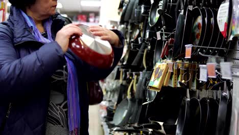 A-mature-woman-chooses-a-cast-iron-frying-pan-in-the-supermarket.