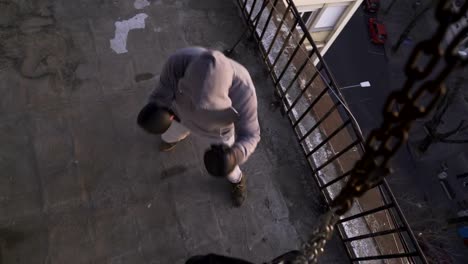 Male-boxer-with-gloves-punches-bag-on-terrace,-chain-close-up,-high-angle-view,-sportsman-practicing,-power-training,-strong-guy-hard-exercising,-strength-exercises,-workout,-handheld,-sunny-day.