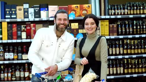 Portrait-of-a-couple-in-a-wine-shop-with-a-full-cart-of-products.