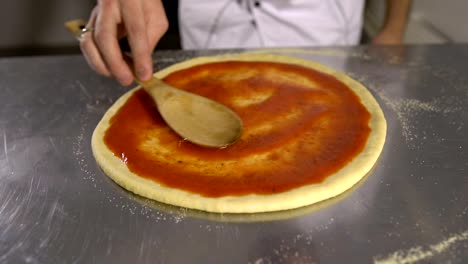 Chef-hand-is-spreading-pasteurized-tomato-paste-onto-a-Pizza-base-close-up