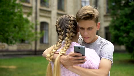 Teenager-using-cell-phone-while-hugging-boyfriend,-absorbed-by-social-networks