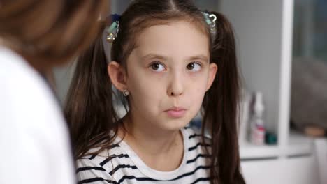 A-woman-physician-examines-a-sore-throat-for-a-little-girl-patient.-Mother-and-young-daughter-at-a-reception-at-the-pediatrician,-close-up.