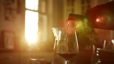 Man-Pouring-Red-Wine-Into-Glass-At-Kitchen-Table