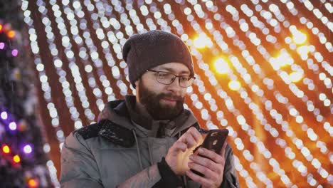 Hombre-barbudo-usar-aplicación-para-smartphone,-luces-de-Navidad