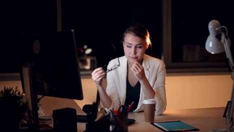 Bastante-joven-Secretario-es-trabajando-en-equipo-por-la-noche-y-luego-sacar-vidrios-y-frotamiento-de-ojos-cansados-y-la-cara-entonces-beber-café-para-llevar.