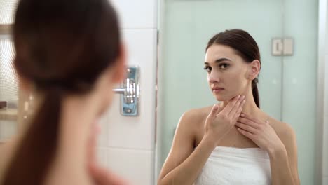 Cuidado-de-la-piel.-Mujer-tocando-la-cara-y-mirando-en-el-espejo-en-el-baño