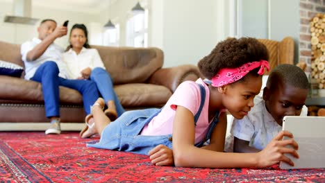 Vista-frontal-de-niños-negro-tendido-en-el-suelo-y-el-uso-de-tableta-digital-en-una-cómoda-casa-4k